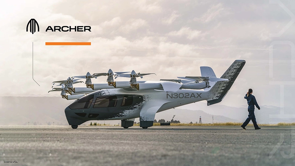A futuristic Archer eVTOL aircraft with six propellers is parked on a runway as a person walks by whilst talking on a mobile.