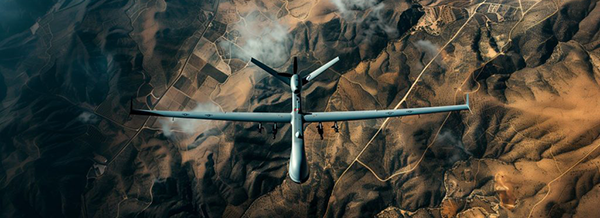Aerial view of a military drone flying over a rugged, mountainous landscape with scattered clouds.